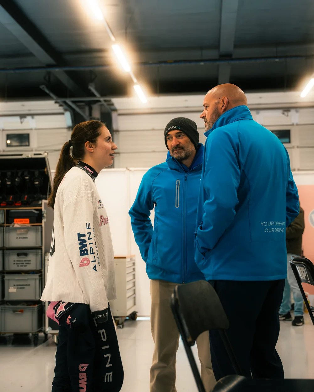 An Aspira driver in conversation with two of the team in the garage, both in Aspira jackets.