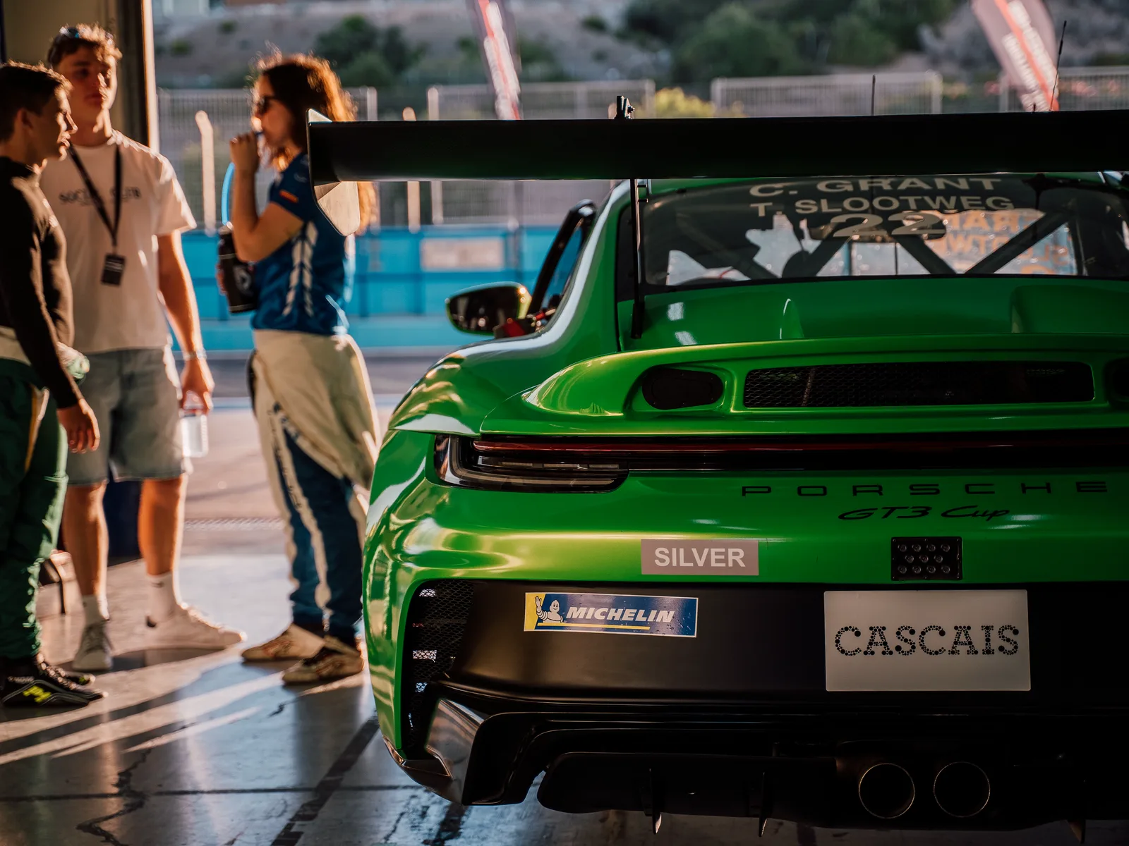 A Porsche 911 GT3 Cup in the garage at Cascais, with drivers and crew in the pit lane outside